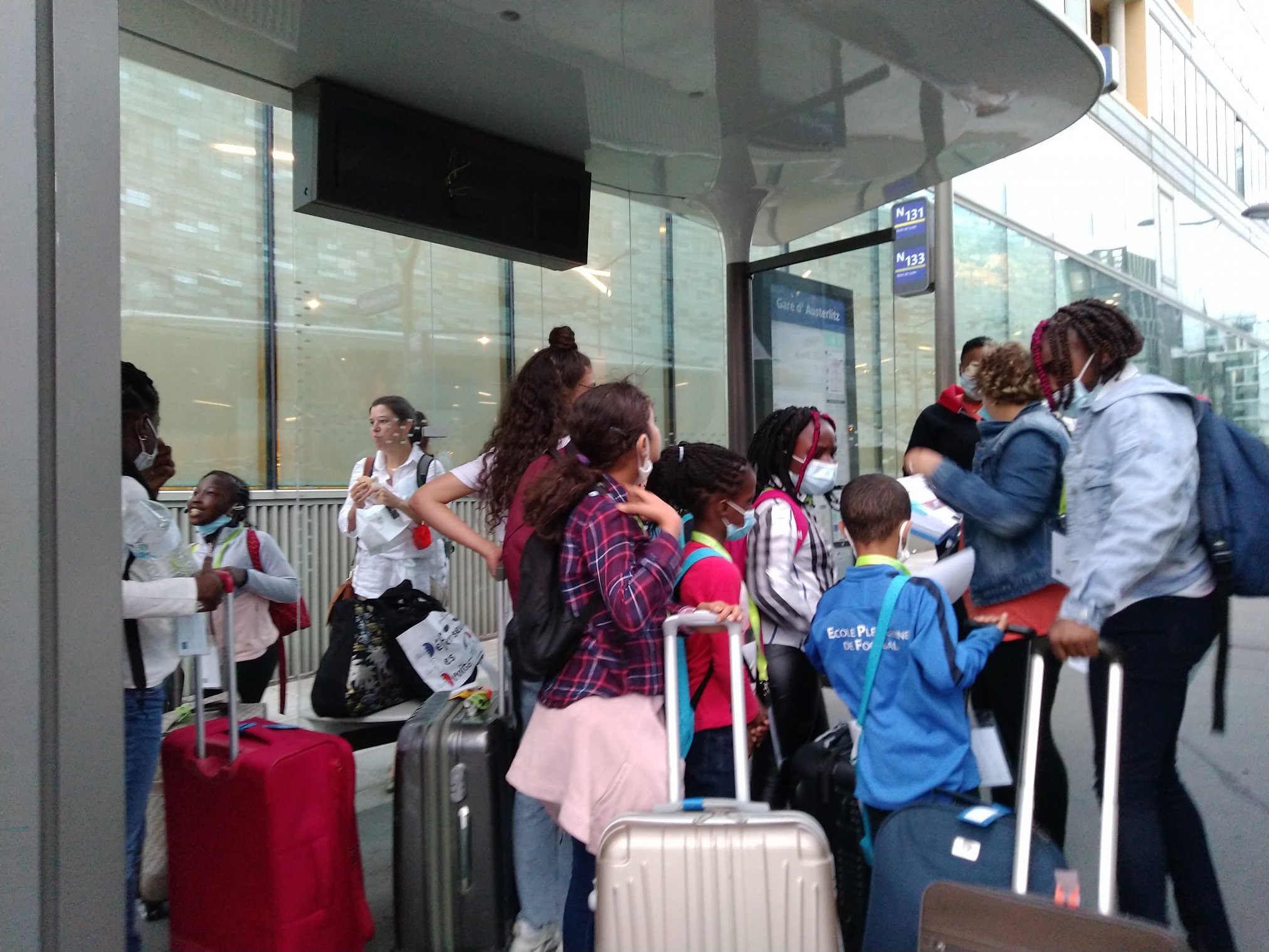 Enfants, accompagnateurs et valises devant l'arrêt du bus. 